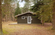Chalet in legno immerso nel bosco a Store Fuglede, Danimarca, visto frontalmente con alberi intorno.