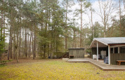 Ferienhaus mit Terrasse und Schuppen im Wald in Store Fuglede, Dänemark, umgeben von hohen Bäumen.
