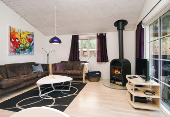 Soggiorno di chalet a Store Fuglede, Danimarca, con camino, divani moderni, arte murale e grandi finestre.