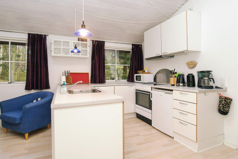 Cocina moderna de chalet con armario blanco, butaca azul y grandes ventanas en Store Fuglede, Dinamarca.
