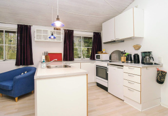 Cuisine moderne de chalet avec armoires blanches, fauteuil bleu et grandes fenĂȘtres Ă Store Fuglede, Danemark.