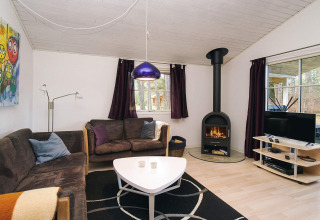 Woonkamer in een chalet in Store Fuglede, Denemarken, met haard, zetels, tv en grote ramen.