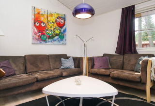 Salon avec canapés bruns, tableau coloré et éclairage moderne dans un chalet de vacances à Store Fuglede.