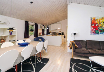 Stue og spisestue i et feriehus i Store Fuglede, Danmark, med moderne møbler og farverig kunst på væggen.
