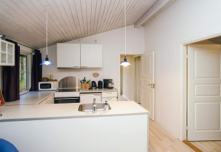 Cocina moderna en una casa de vacaciones en Store Fuglede, Dinamarca, con armarios blancos y luces azules.