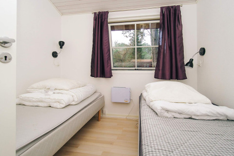 Slaapkamer met twee enkele bedden, paarse gordijnen en raam in 6-persoons chalet in Store Fuglede, Denemarken.