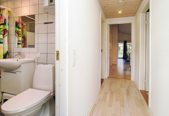 Corridoio con pavimento in legno chiaro e bagno piastrellato in uno chalet a Store Fuglede, Danimarca, per sei.