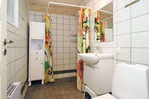 Moderne badkamer met witte tegels, kleurrijk douchegordijn en houten plafond in vakantiehuis Store Fuglede.
