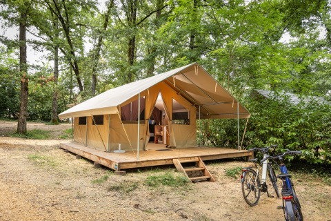 Safari tent Bungalow Classic op een houten platform in het bos, met fietsen geparkeerd bij de ingang.