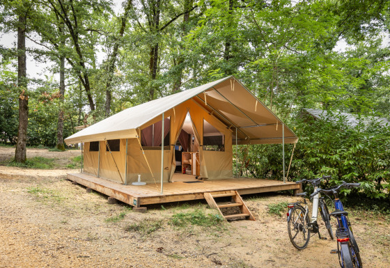 Safari tent Bungalow Classic op een houten platform in het bos, met fietsen geparkeerd voor de tent.