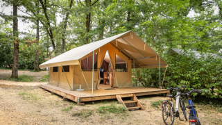Tienda safari Bungalow Classic sobre tarima de madera en el bosque, con bicicletas aparcadas delante.