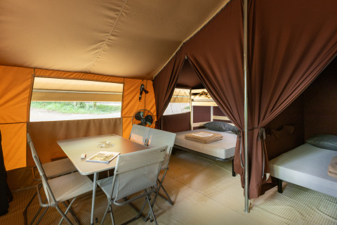Interior of a safari bungalow tent with dining table, chairs, and beds at Huttopia Chardons Bleus in France.