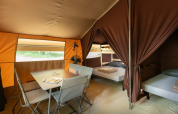 Binnenkant van een safari-bungalowtent met tafel, stoelen en bedden bij Huttopia Chardons Bleus, Frankrijk.