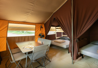 Binnenkant van een safari-bungalowtent met tafel, stoelen en bedden bij Huttopia Chardons Bleus, Frankrijk.