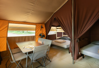 Interior de una tienda safari tipo bungalow con mesa, sillas y camas en Huttopia Chardons Bleus, Francia.