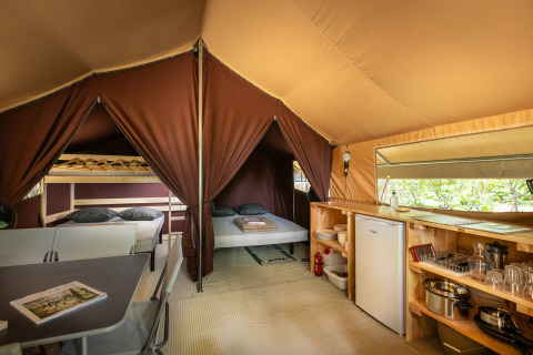 Interior view of a safari bungalow tent with double bed, kitchenette, and bunk beds at Huttopia Chardons Bleus.