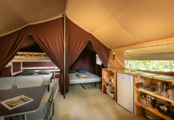 Binnenzicht van een safari bungalowtent met tweepersoonsbed, keukenhoek en stapelbedden bij Huttopia Chardons Bleus.