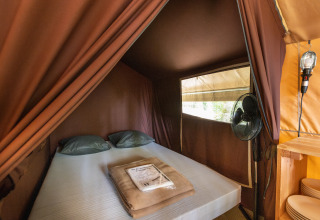 Interior view of a Bungalow tent Classic with double bed, fan, and soft lighting at a campsite.