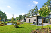 Moderne lodge aan een vijver omringd door groen op Holiday Park De Lochemse Berg in Nederland, zonnige dag.