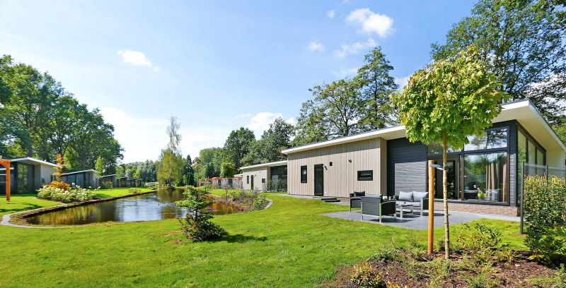 Moderne Lodge am Teich im Holiday Park De Lochemse Berg in den Niederlanden, umgeben von grüner Natur.