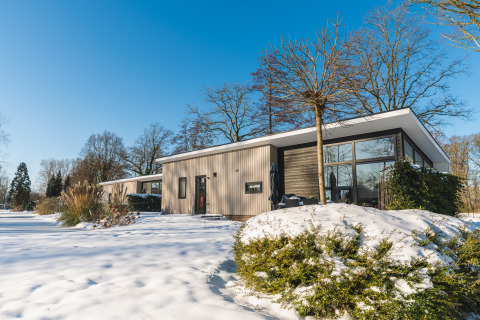 Lodge Grand Modern, een moderne lodge met grote ramen, gelegen in een besneeuwd en bosrijk landschap.