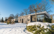 Lodge Grand Modern, pavillon moderne aux larges baies vitrées, entouré de neige et d’arbres dépouillés.