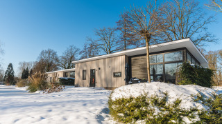 Lodge Grand Modern, una casa moderna de madera con grandes ventanales, rodeada de nieve y árboles.