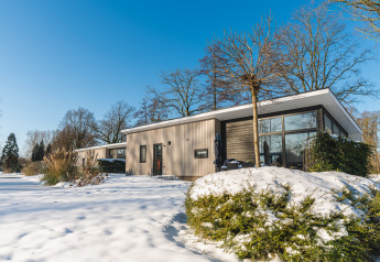 Lodge Grand Modern, pavillon moderne aux larges baies vitrées, entouré de neige et d’arbres dépouillés.