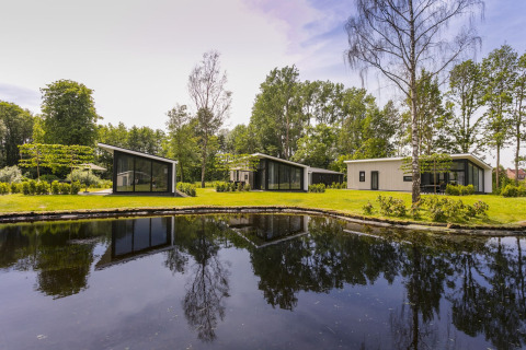 Moderne Lodges am Teich im Holiday Park De Lochemse Berg, umgeben von Bäumen in den Niederlanden.