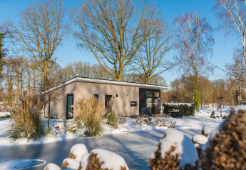 Lodge Grand Modern bij Vakantiepark De Lochemse Berg in Nederland, omgeven door sneeuw en bomen.