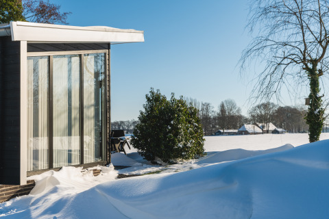 Lodge Grand Modern en Holiday Park De Lochemse Berg, Países Bajos, rodeado de nieve bajo el sol invernal.