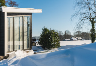 Lodge Grand Modern en Holiday Park De Lochemse Berg, Países Bajos, rodeado de nieve bajo el sol invernal.