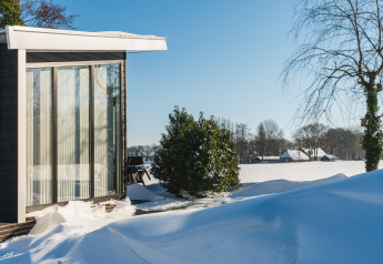 Lodge Grand Modern en Holiday Park De Lochemse Berg, Países Bajos, rodeado de nieve bajo el sol invernal.