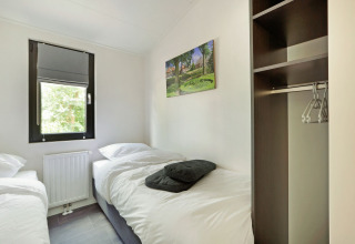 Dormitorio luminoso con dos camas individuales, ventana, armario abierto y cuadro en Lodge Grand Modern, De Lochemse Berg.