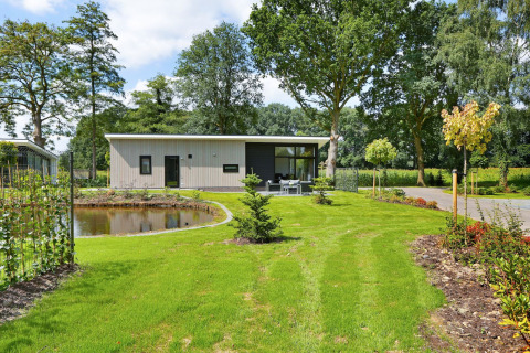 Die Lodge Grand Modern im Holiday Park De Lochemse Berg, Niederlande, mit Garten und Teich im Vordergrund.