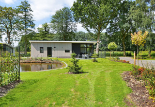Lodge Grand Modern au Holiday Park De Lochemse Berg, Pays-Bas, entouré d’un jardin verdoyant et d’un étang.