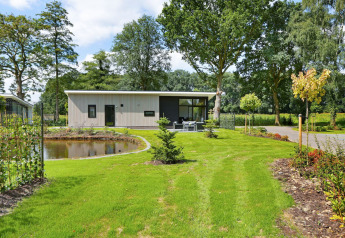 Lodge Grand Modern au Holiday Park De Lochemse Berg, Pays-Bas, entouré d’un jardin verdoyant et d’un étang.