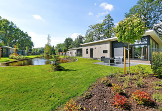 Moderne lodge bij een vijver in Holiday Park De Lochemse Berg, Nederland, omgeven door groen.