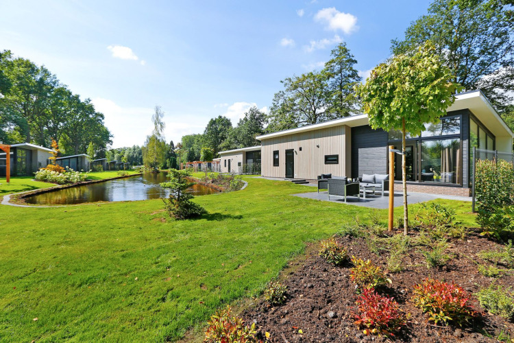 Moderne Lodge am Teich im Holiday Park De Lochemse Berg in den Niederlanden, umgeben von viel Grün.