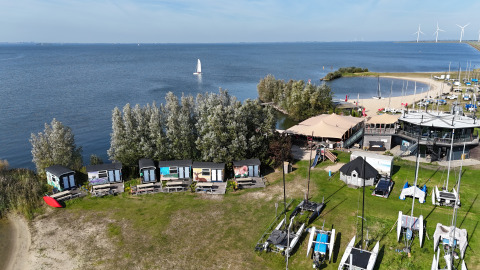 Luftfoto af Tiny Wagon lodge ved Marina Parcs Almere, Holland, med hytter langs søbredden.