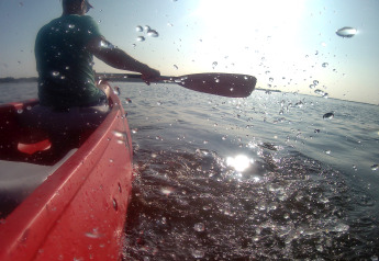 Persona che rema in canoa rossa al Tiny Wagon di Marina Parcs Almere, Olanda, con sole e schizzi d'acqua.