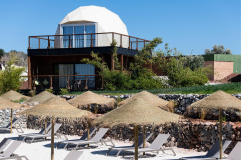 Dome ‘House Duplex Do Lago’ bij Wecamp Reserva Alecrim in Portugal met ligstoelen en rieten parasols aan het strand.