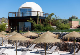 Dome ‘House Duplex Do Lago’ bij Wecamp Reserva Alecrim in Portugal met ligstoelen en rieten parasols aan het strand.