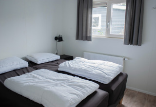 Soveværelse i Veluwelodge XL på Recreation park De Boshoek, med to senge, hvidt sengetøj og vindue.