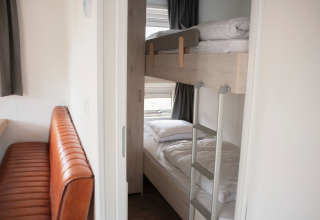 Blik in een compacte kamer met stapelbedden en een bruine lederen bank in Veluwelodge XL, De Boshoek.