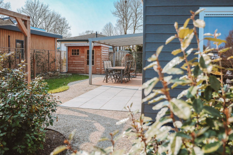 Gartenbereich mit Terrasse, Gartenhaus und moderner Bepflanzung bei Veluwelodge XL im De Boshoek Park, Niederlande.