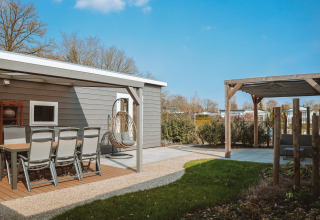 Udendørs opholdsområde ved Veluwelodge XL på Rekreatiepark De Boshoek, Holland, med spisebord og have.