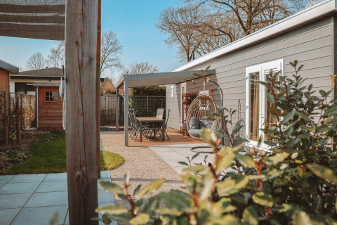 Terrasse der Veluwelodge XL mit Gartenmöbeln, Hängesessel und Blick auf schön gestaltete Pflanzen.