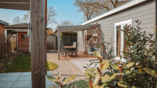 Udendørs terrasse ved Veluwelodge XL med havemøbler, hængestol og udsigt til grønne planter.