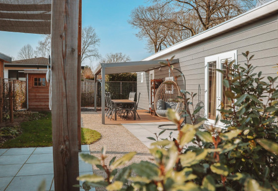 Buitenterras aan Veluwelodge XL met tuinmeubilair, hangstoel en zicht op groene beplanting.